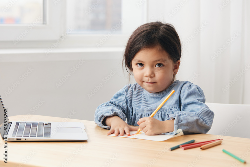 a cute, pleasant little girl up to school age sits at a table and draws with colored pencils. Themes of hobby, development and training a cute, pleasant little girl up to school age sits at a table and draws with colored pencils. Themes of hobby, development and training