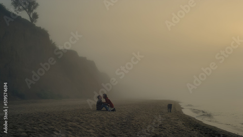 Young couple relaxing on beach at sunrise. Boyfriend and girlfriend kissing 