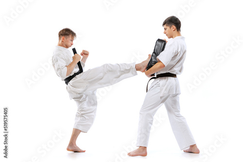 Two athletes, karate-do fighters in doboks practicing karate isolated on white background. Concept of sport, education, skills, martial arts, healthy lifestyle