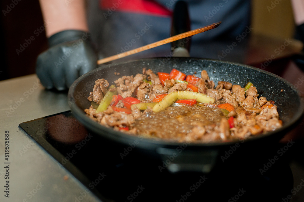 Cook fries meat in a pan with vegetables. Cook fries meat in a pan with vegetables.