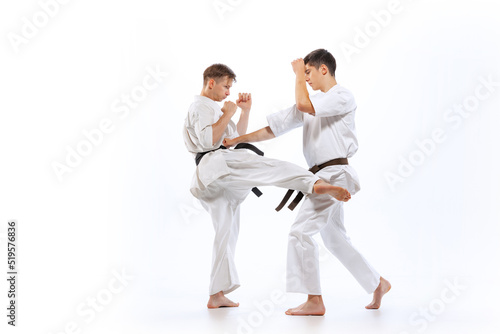 Two athletes, karate-do fighters in doboks practicing karate isolated on white background. Concept of sport, education, skills, martial arts, healthy lifestyle