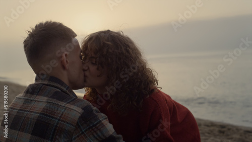 Romantic couple kissing on beach at sunrise. Woman and man looking at each other