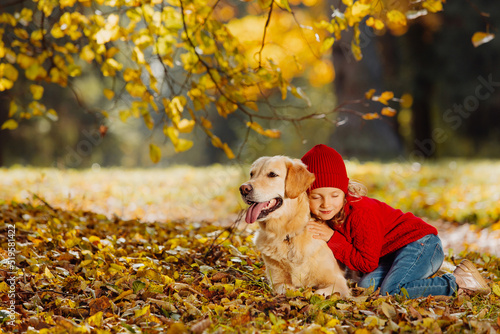 A child and a dog lie together on autumn leaves and look ahead. Warm colors of autumn in the park.