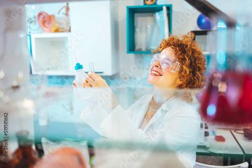 Female scientist working in the lab. A female medical or scientific researcher or woman doctor looking at a test tube of clear solution in a laboratory with her microscope beside her.