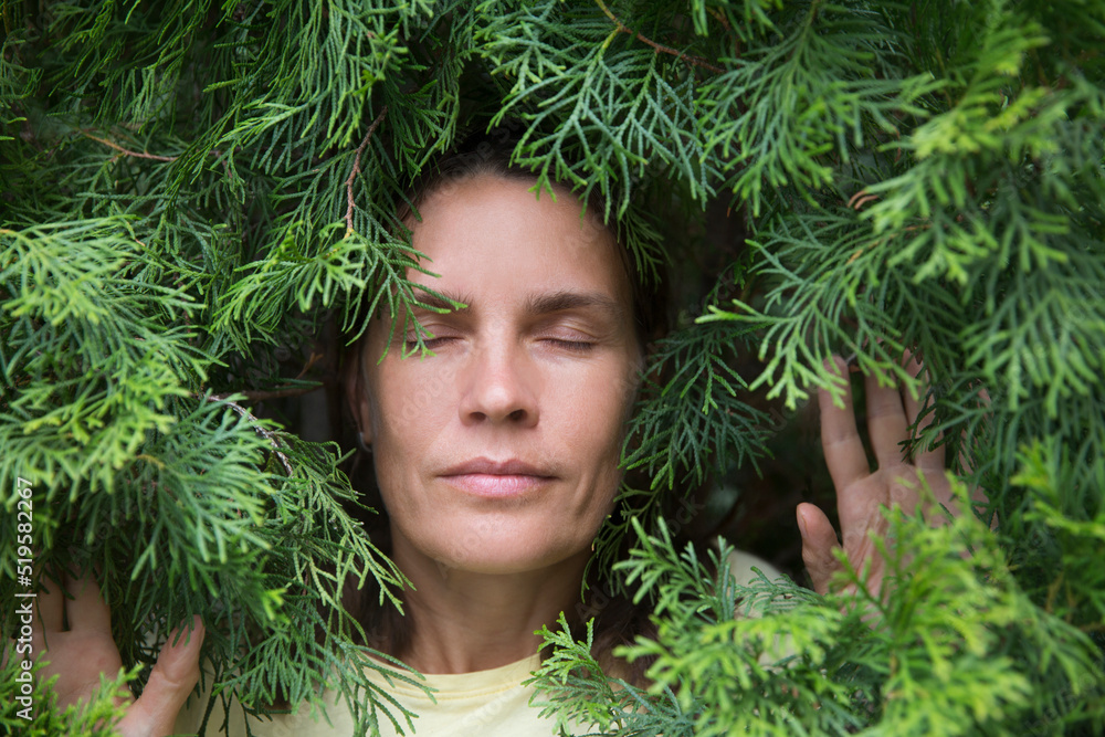 Profile of a enjoying nature middle aged woman to stand in thuja branches breathing fresh air. celebrate earth's day. Aromatherapy and Spa concept. ecology. climate change Profile of a enjoying nature middle aged woman to stand in thuja branches breathing fresh air. celebrate earth's day. Aromatherapy and Spa concept. ecology. climate change