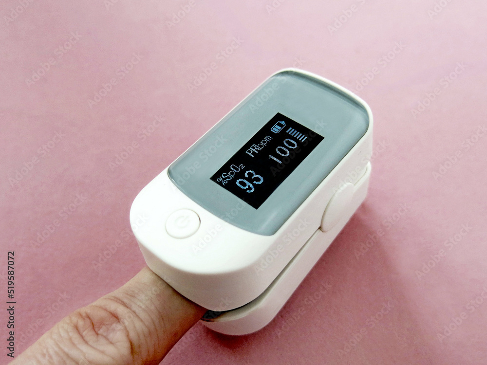 Finger with a pulse oximeter on a pink background close-up. Low saturation on display Finger with a pulse oximeter on a pink background close-up. Low saturation on display