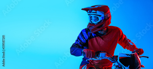 Photography Portrait of young man, biker in helmet posing on motorbike isolated over blue studio background in neon light