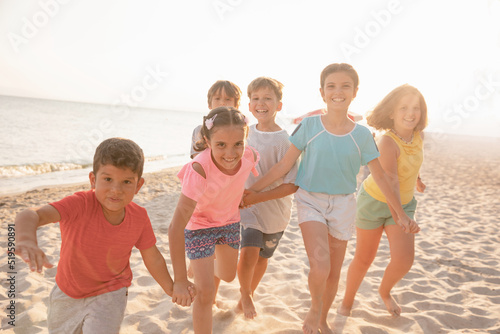 Happy children running on the beach at sunset. Cheerful kids having good time at summer holidays. Smiling boys and girls on vacation on seashore.