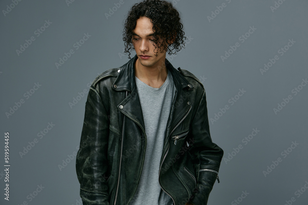 Fototapeta premium Serious adorable stylish tanned curly man leather jacket looks aside posing isolated on over gray studio background. Cool fashion offer. Huge Seasonal Sale New Collection concept. Copy space for ad