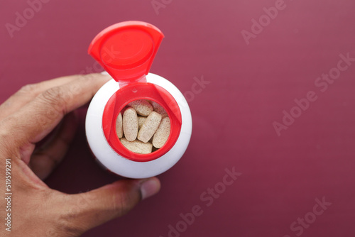young man hand holding medicine pill container on red background top view 