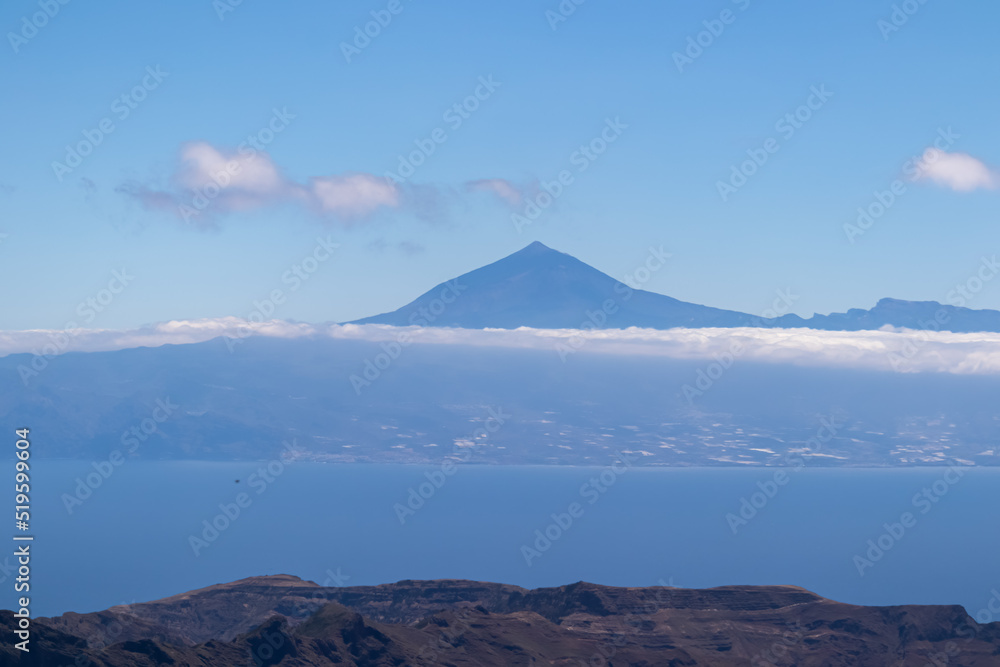 Scenic view on cloud covered volcano mountain peak Pico del Teide on Tenerife seen from Mirador Morro de Agando, La Gomera, Canary Islands, Spain, Europe. Lookout near Roque de Agando. Atlantic Ocean