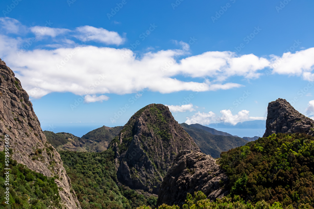 Obraz premium Massive volcanic rock formations in Garajonay National Park seen from Roque de Agando, La Gomera, Canary Islands, Spain, Europe. Hiking trail over hills covered by forest and tropical fauna in summer