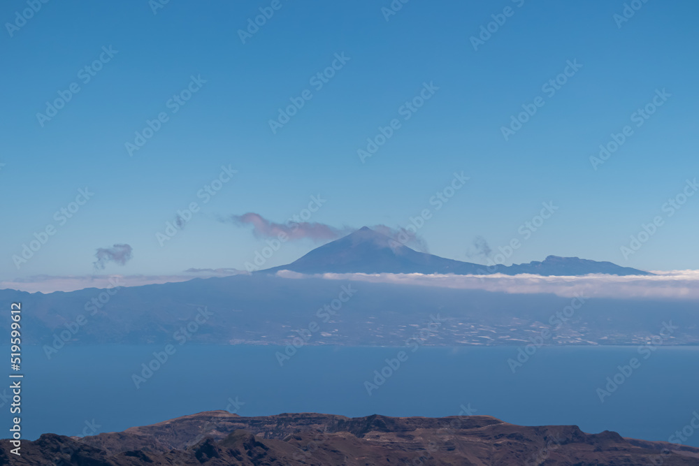 Scenic view on cloud covered volcano mountain peak Pico del Teide on Tenerife seen from Mirador Morro de Agando, La Gomera, Canary Islands, Spain, Europe. Lookout near Roque de Agando. Atlantic Ocean