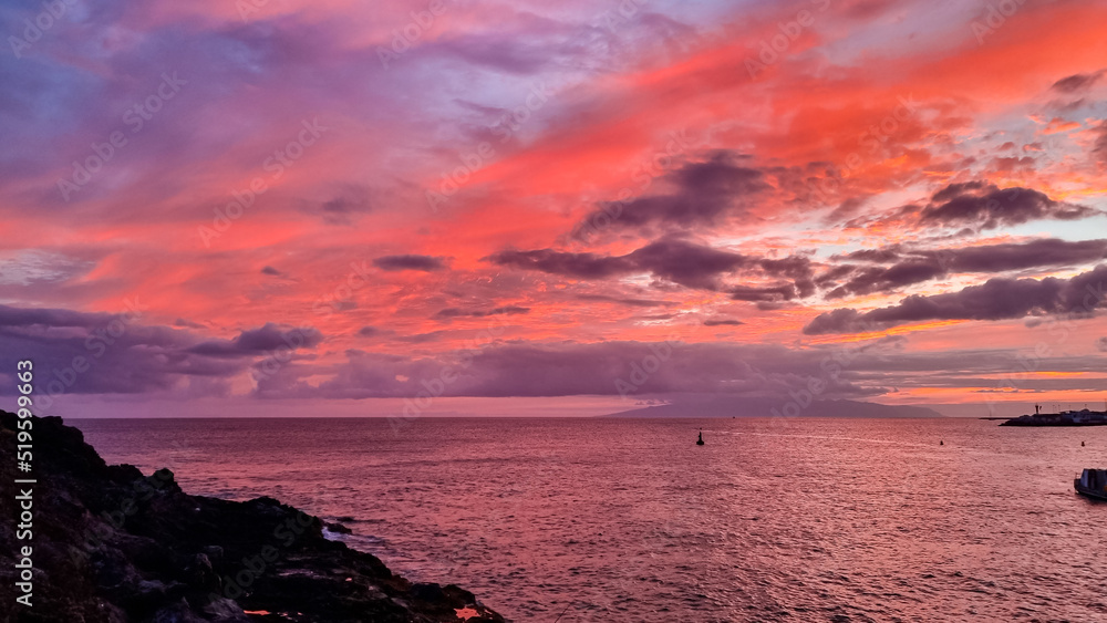 Romantic sunset over the sea in summer seen from lookout Cypelek Los Cristianos, Tenerife, Canary Islands, Spain, Europe. Vibrant colours of the clouds. Vacation vibes on the Atlantic Ocean. Awe