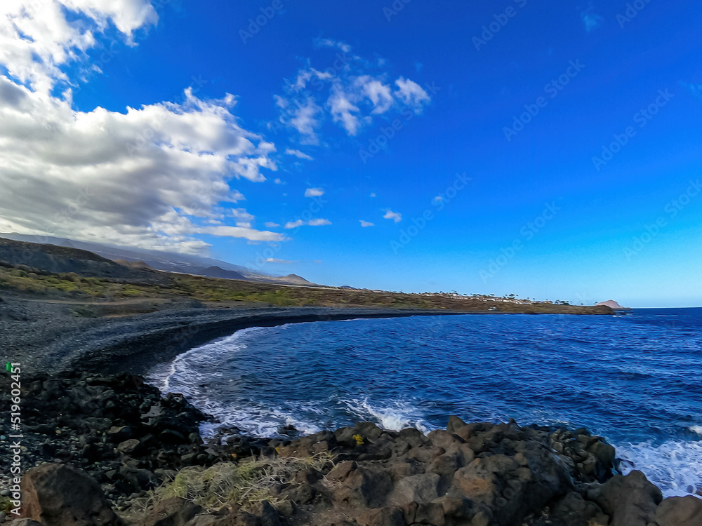 Scenic view on black stone pebble beach Playa Colmenares near Amarilla, Golf del Sur, Tenerife, Canary Islands, Spain, Europe. Vacation resort complex. Waves from Atlantic Ocean. Montana Roja in back Scenic view on black stone pebble beach Playa Colmenares near Amarilla, Golf del Sur, Tenerife, Canary Islands, Spain, Europe. Vacation resort complex. Waves from Atlantic Ocean. Montana Roja in back