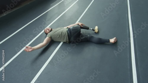 High angle shot of professional sportsman with prosthetic leg doing supine spinal twist pose while having post workout stretch in indoor stadium photo