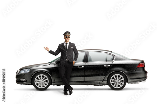 Chauffeur in a black suit showing with hand and leaning on a black car © Ljupco Smokovski