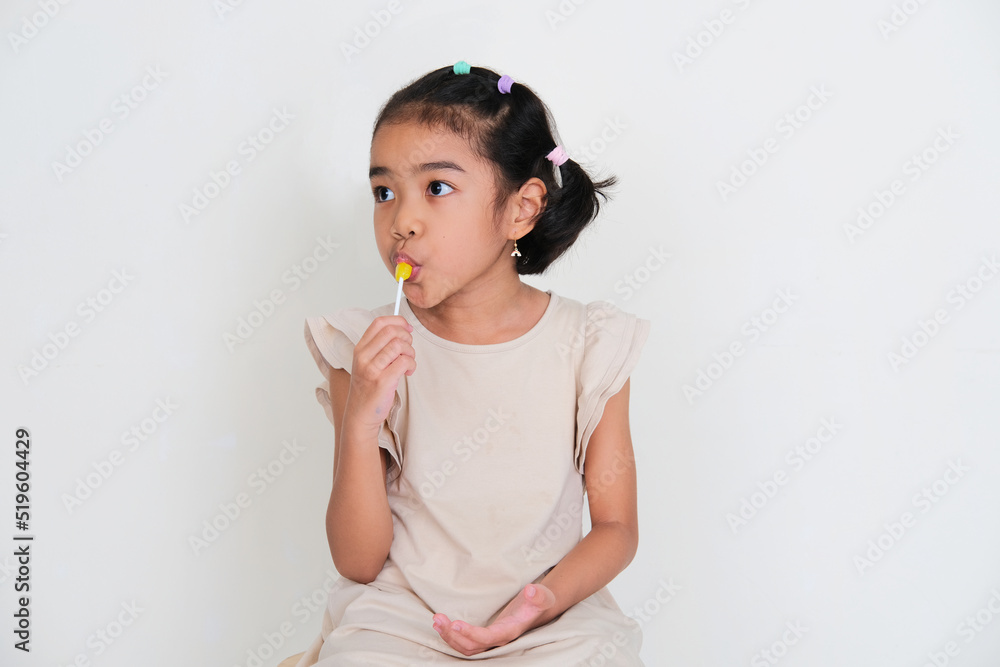 Asian little girl eating yellow lollipop candy Asian little girl eating yellow lollipop candy