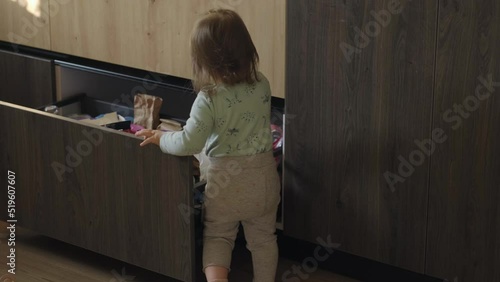 Curious baby girl exploring the drawer in the kitchen and selecting food. Childcare concept. Baby development. Baby care. photo