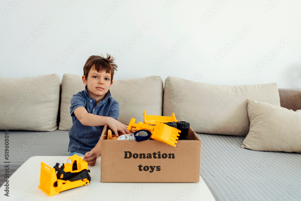 Adorable boy holding cardboard donation box full with folded clothes and toys. Adorable boy holding cardboard donation box full with folded clothes and toys.