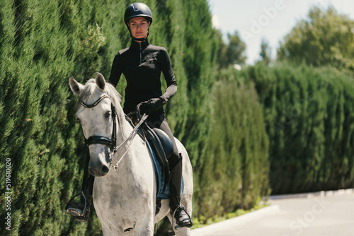 Equestrian sport. Portrait of young woman, female rider training at riding arena in summer day, outdoors. Dressage of horses. Horseback riding