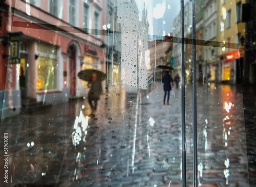 Rainy city street people silhouette with umbrellas Rainy weather season Autumn leaves on window rain drops ,night blurred light reflection cold urban defocus background 