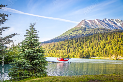 Red float plane parked on the waters of Upper Trail Lake on the Kenai Peninsula of Alaska USA framed by pine trees with blurred mountains with snow above the tree line in the background photo