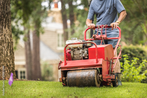 Man using gas powered aerating machine to aerate residential grass yard. Groundskeeper using lawn aeration equipment for turf maintenance. photo