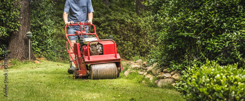 Man using gas powered aerating machine to aerate residential grass yard. Groundskeeper using lawn aeration equipment for turf maintenance. photo