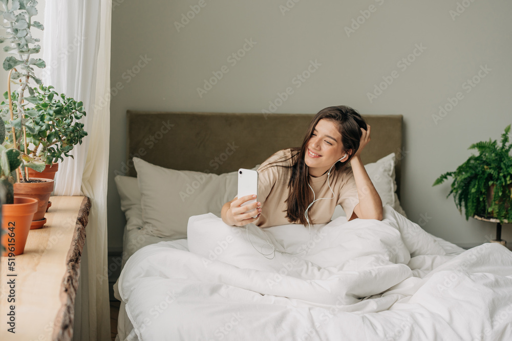 A girl in her twenties is sitting on the bed in the morning chatting on a video call on the phone. A girl in her twenties is sitting on the bed in the morning chatting on a video call on the phone.