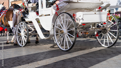 Photography A white horse-drawn carriage with tourists on a gray cobbled street of the old town on a sunny day among the townspeople and tourists of Krakow