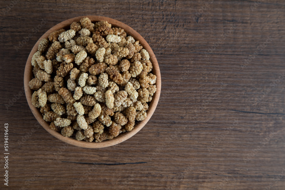 Bowl full of dried mulberry on a wooden background
