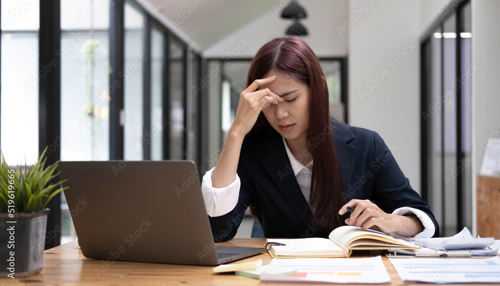 Young Asian woman feeling migraine head strain. Tired, Overworked businesswoman financier while working on laptop computer in office. Young Asian woman feeling migraine head strain. Tired, Overworked businesswoman financier while working on laptop computer in office.