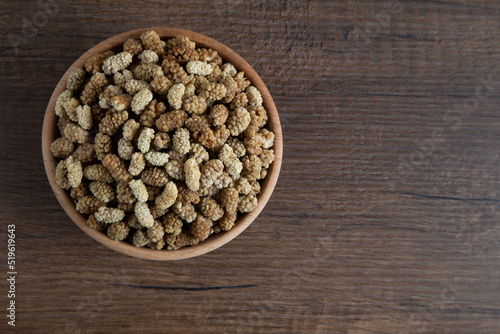 Bowl full of dried mulberry on a wooden background 