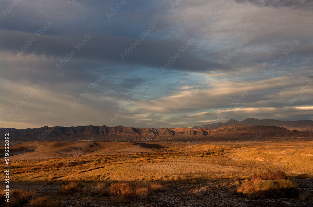 Landscape image taken at Tecopa in the Mojave Desert, California. The photo shows sunset clouds, a mountain range, and badlands. Tecopa is known for its natural warm springs.