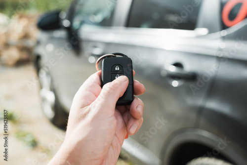 Car alarm. Close-up of human hand using remote key of car, pressing open button. Selective focus on remote control, black car in bokeh