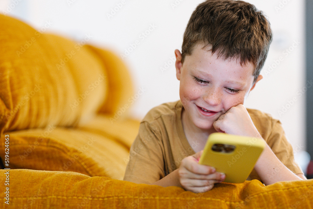 Happy boy lying on a sofa browsing on smartphone