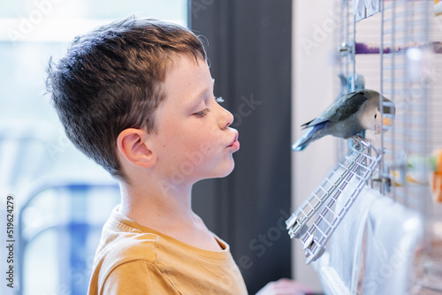 Close-up of a boy whistling to a parakeet inside the cage photo