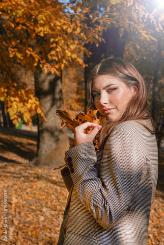  Smilng dreaming young woman at autumn park. Autumn mood  Woman holding in her hands yellow maple leaves.