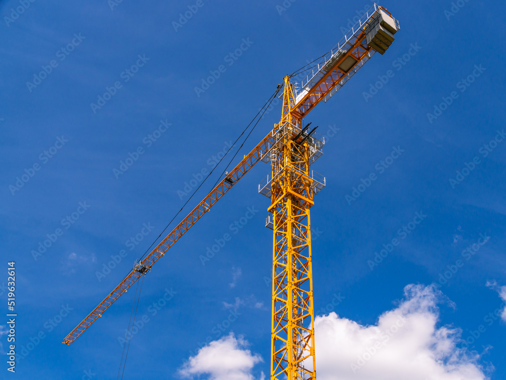 A tower construction crane on the background of a blue sky with clouds. Boom rotary crane with boom. Construction of apartment buildings in the city. Construction of high-rise buildings. A tower construction crane on the background of a blue sky with clouds. Boom rotary crane with boom. Construction of apartment buildings in the city. Construction of high-rise buildings.