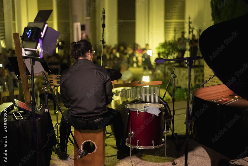 young man playing drums at an open-air evening concert with the audience in the background