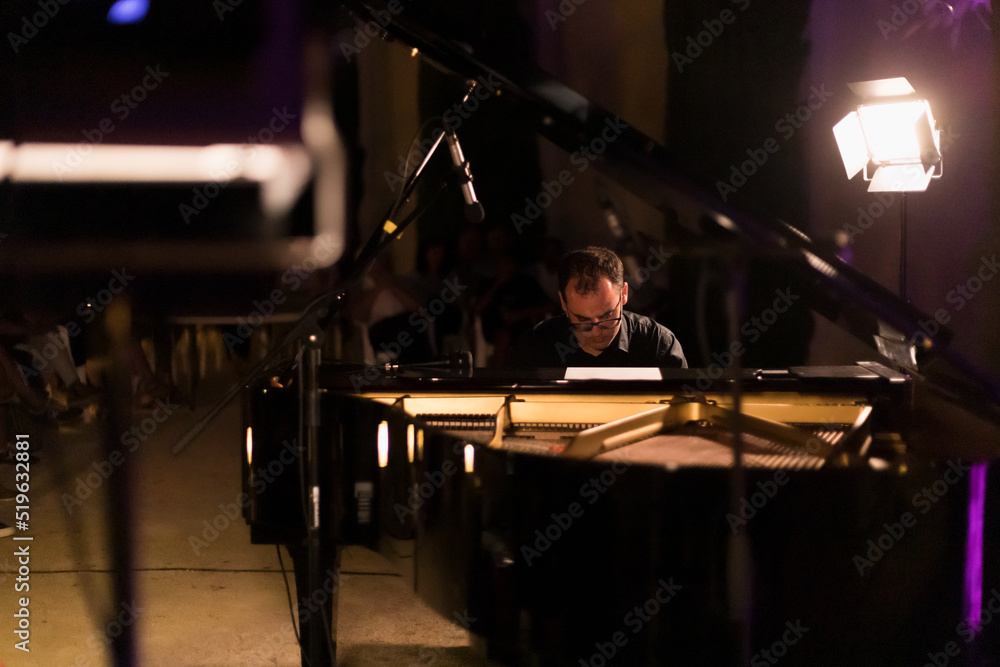 man playing grand piano at a night concert, general shot, between the spotlights
