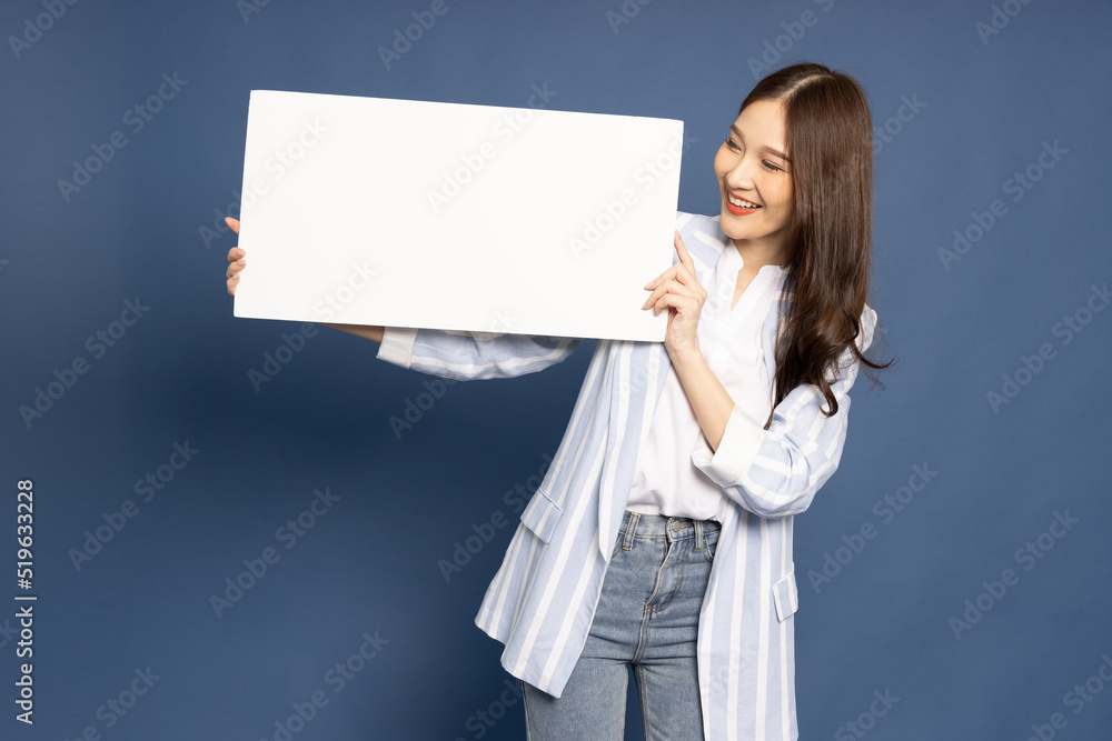 Young Asian business woman showing and holding blank white billboard isolated on blue background Young Asian business woman showing and holding blank white billboard isolated on blue background