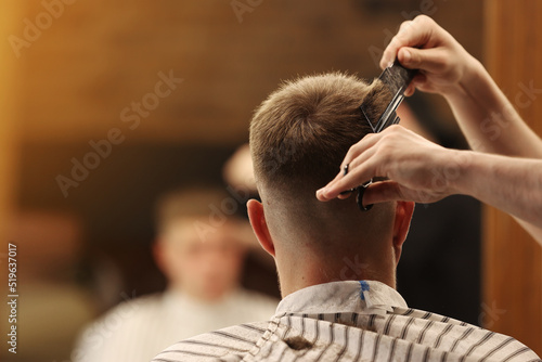 A young male Barber adjusts the hair of a male client. Professional hair care products. Cinematic close-up of a barber giving fade haircut to male client. shot of short clipper hairstyle