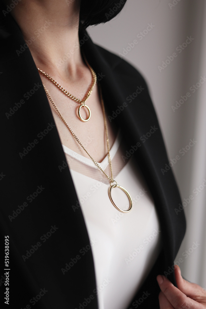 Decoration on a woman's neck. A woman in a black jacket and white blouse, cropped view. Stylish double golden chain with circles Decoration on a woman's neck. A woman in a black jacket and white blouse, cropped view. Stylish double golden chain with circles