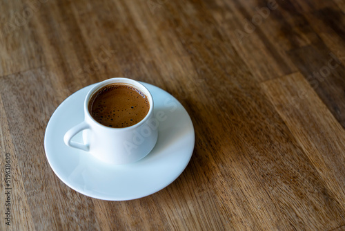 Selective focus on a white cup of  turkish coffee on wooden table background with copy space. Noise effect and grainy texture.