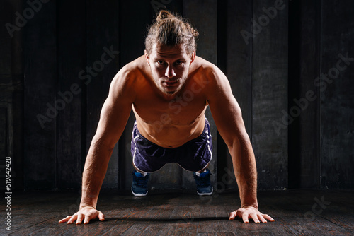Young athletic guy in blue shorts on floor doing plank exercise on floor. Active strong fit sportsman do push-ups workout at gym with naked torso ripped shoulders. Sportive man, male, runner training