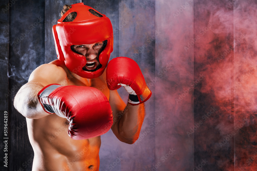 Dynamic motion portrait of sportive muscular athletic man in boxer gloves, helmet and shorts practicing attack. Fit strength male fighter kickboxing engaged in gym with screaming face in movement. - obrazy, fototapety, plakaty 