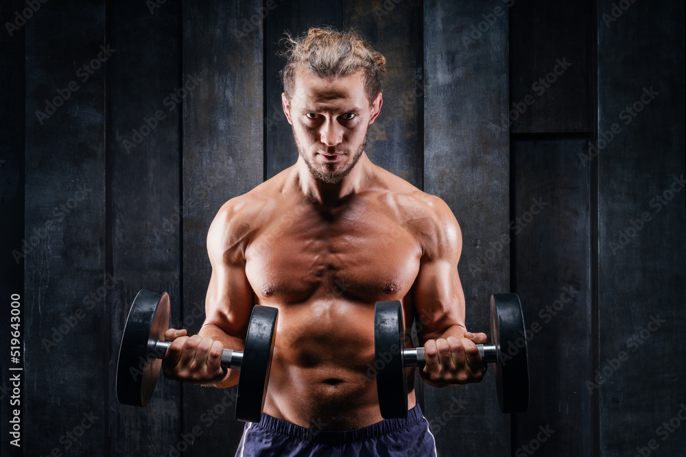 Fitness in gym, sport and healthy lifestyle concept. Handsome athletic man with naked torso making lifting exercises for bigger biceps. Bodybuilder male trains deltoid muscles with dumbbells.