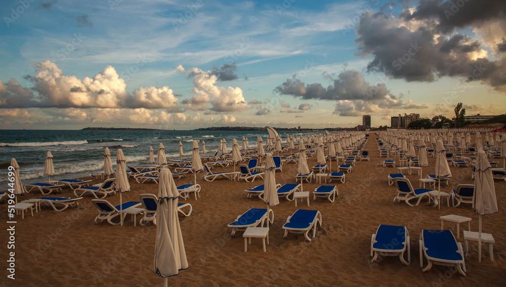 Loungers on sandy beach by the sea on a dramatic sky, end of season in resort, Bulgaria Loungers on sandy beach by the sea on a dramatic sky, end of season in resort, Bulgaria